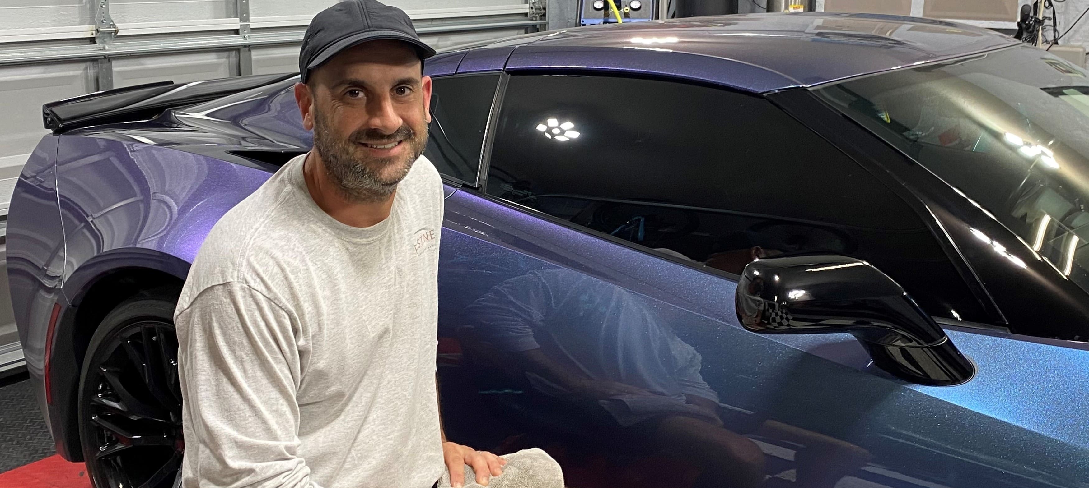 A man standing in front of a blue car.